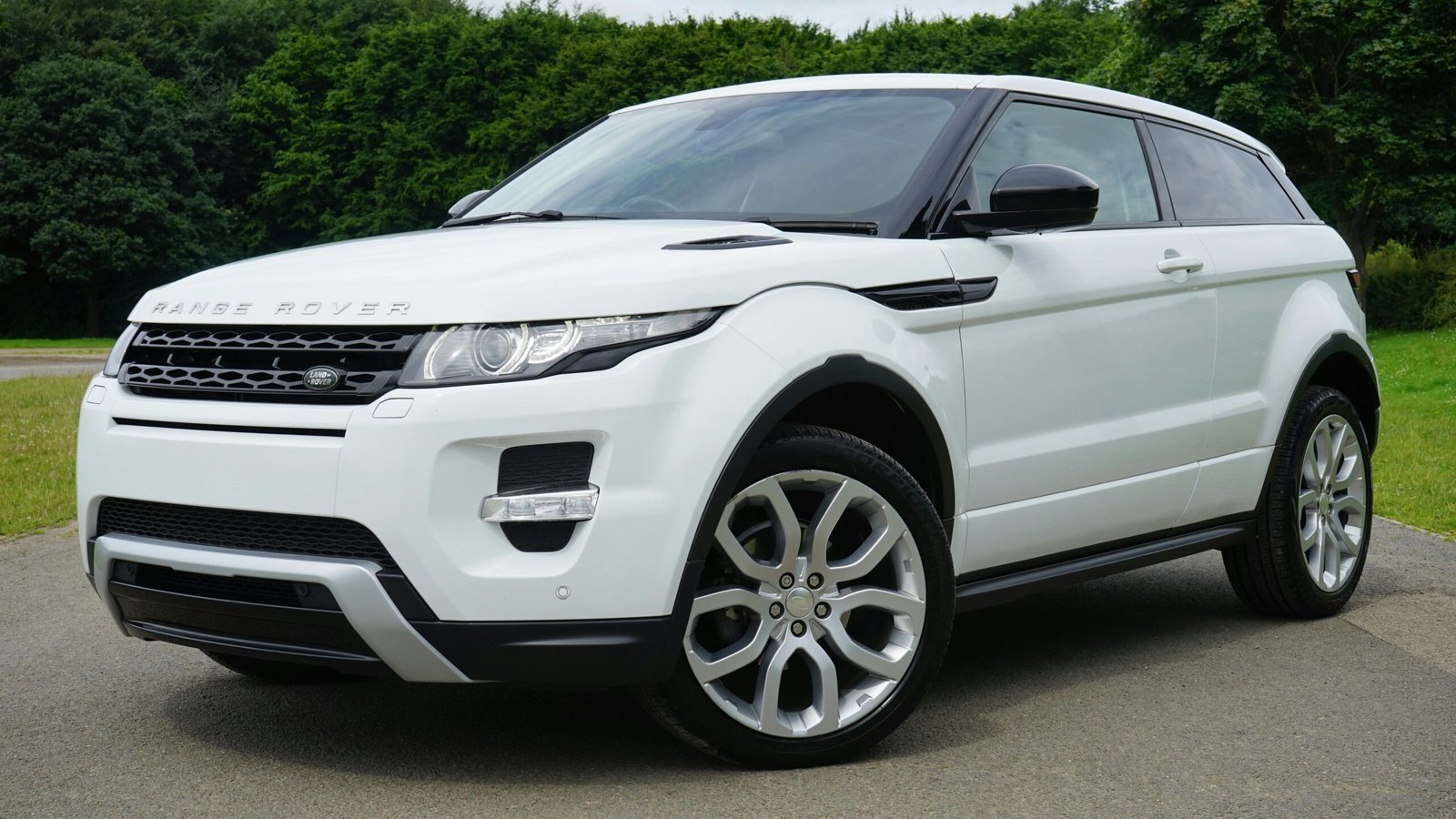 Home Stylish white Range Rover parked on a road in a green outdoor setting, showcasing its luxury design.