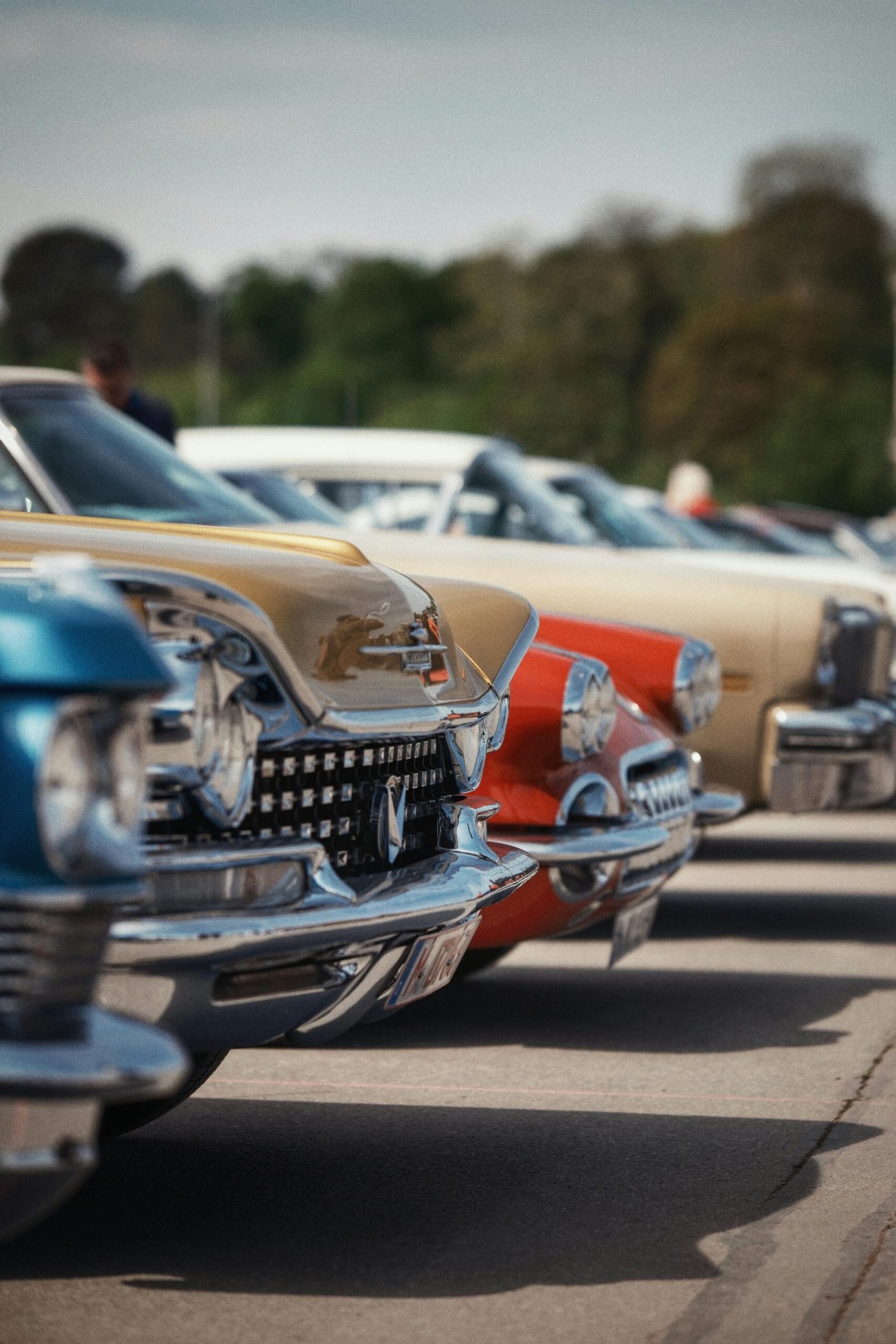 Home Colorful vintage cars lined up in perfect alignment at an outdoor car show under a clear sky.
