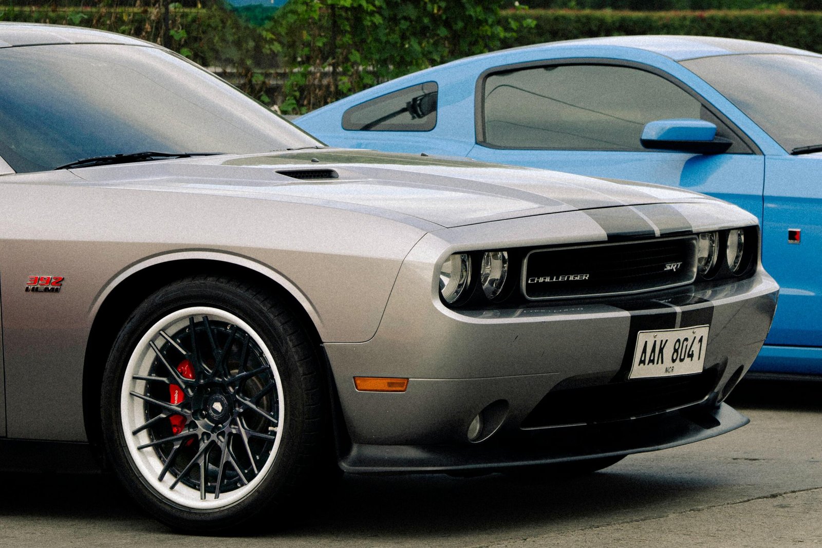 Services Silver Dodge Challenger and blue Ford Mustang parked outdoors, showcasing automotive design.