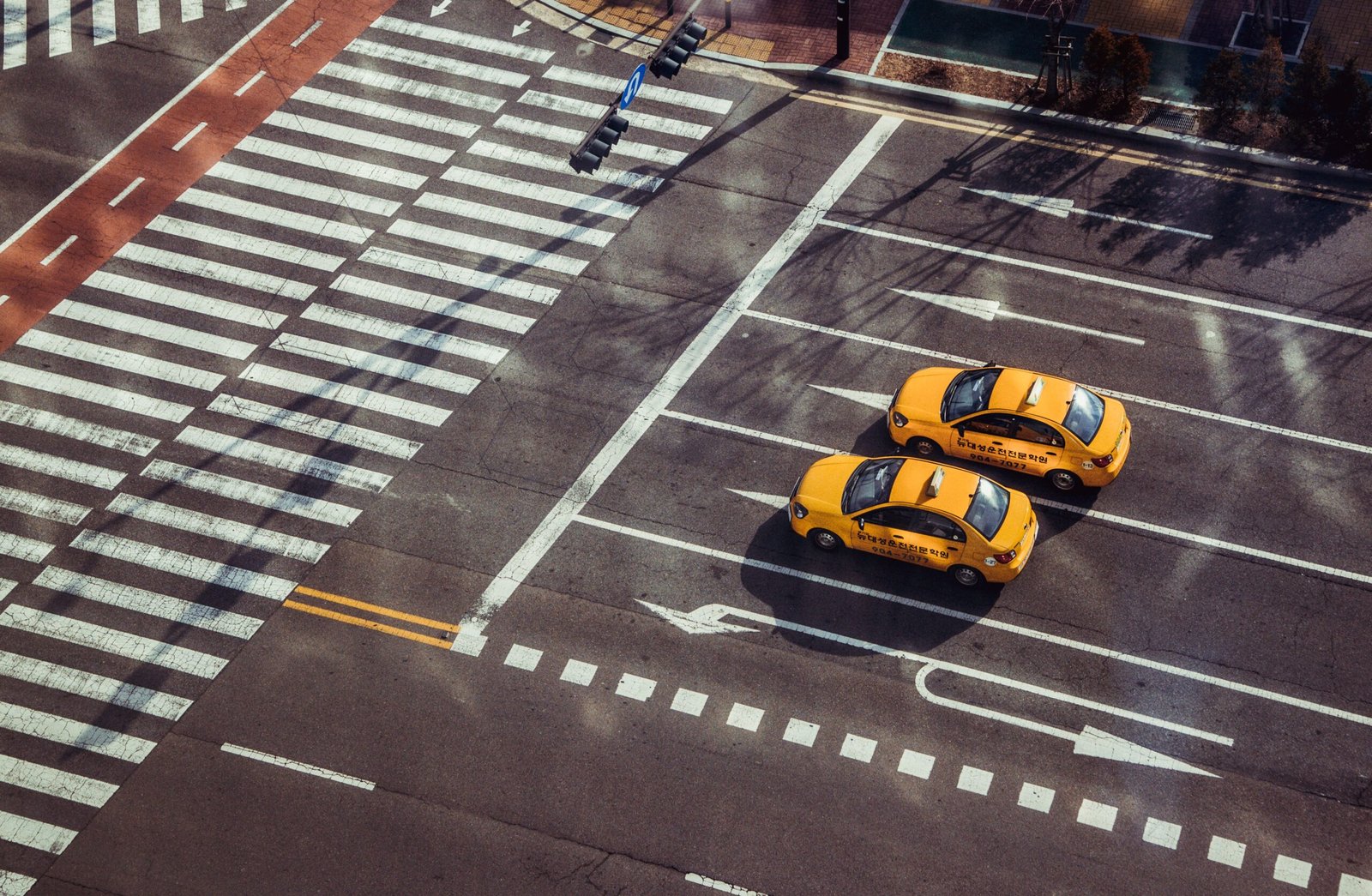 Two yellow taxis navigate a city intersection with marked pedestrian crossings.