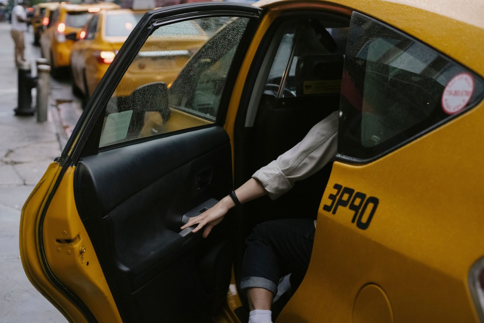 Anonymous passenger closing door of cab parked on roadside with blurred cars on background in rush hour on street in city