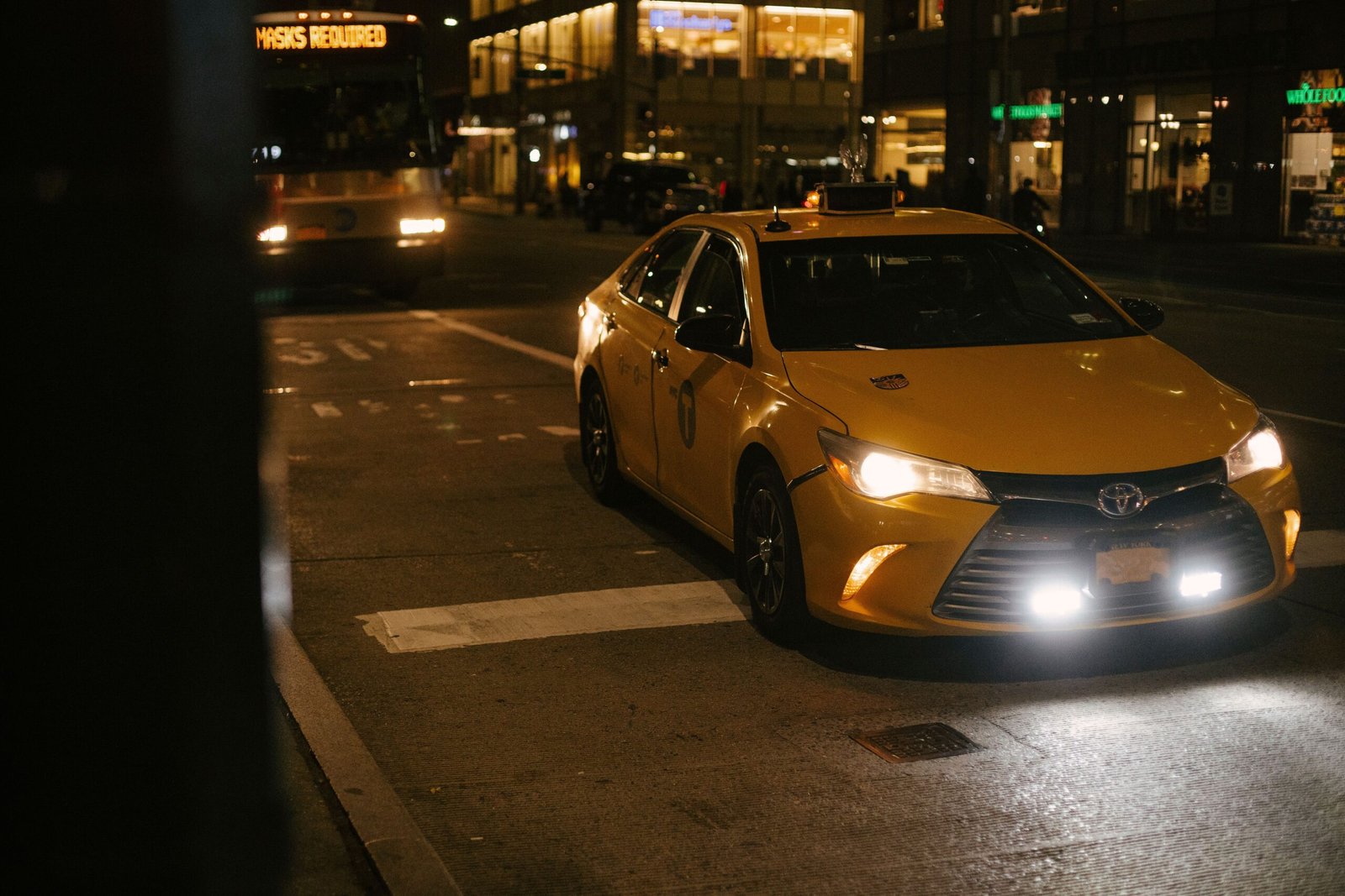 High angle of modern yellow cab and bus with glowing headlights driving on city street in evening
